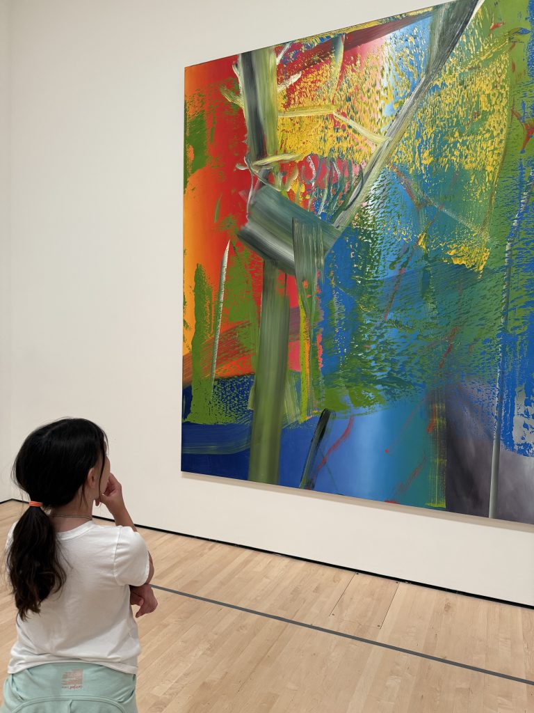 a girl stands in front of a colorful painting