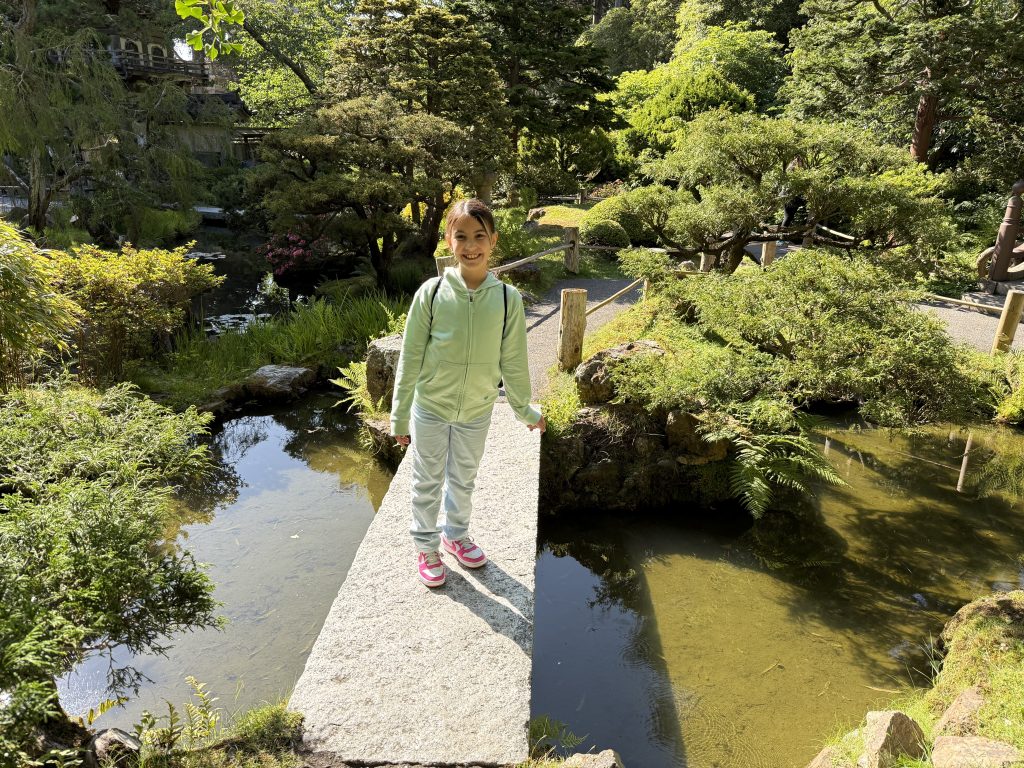 a girl walks across a stone bridge in the middle of a garden