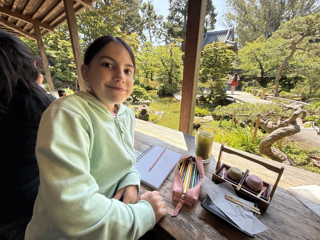a girl sits in front of a koi pond in the middle of a garden