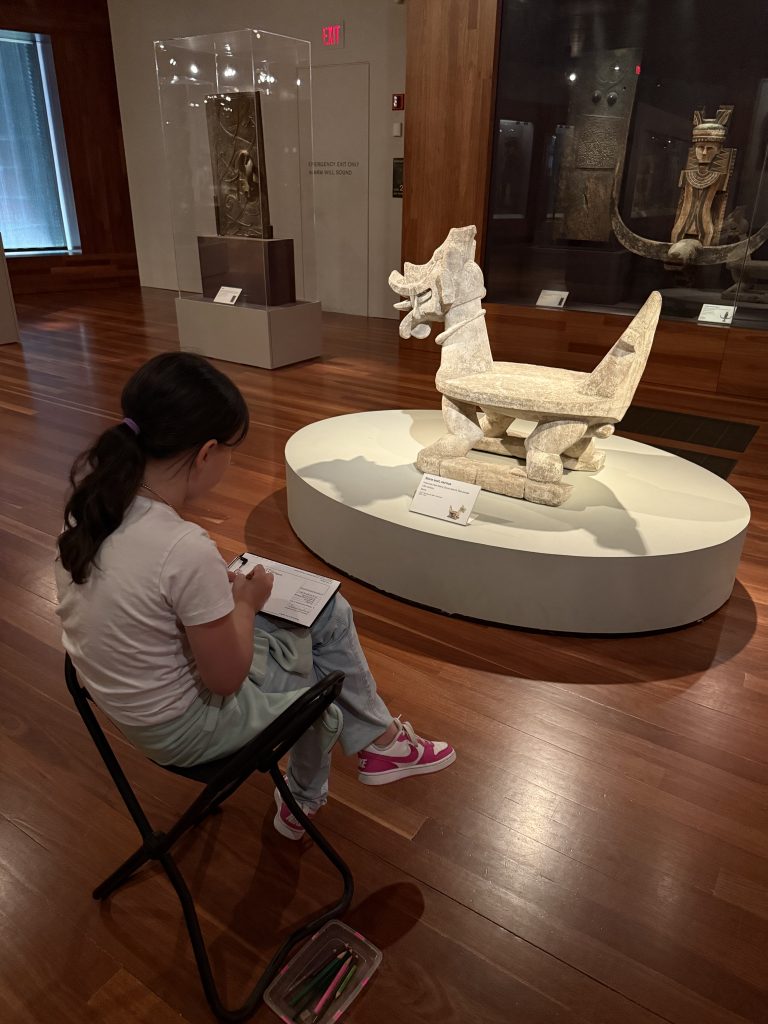 a girl sits on a stool in front of a statue