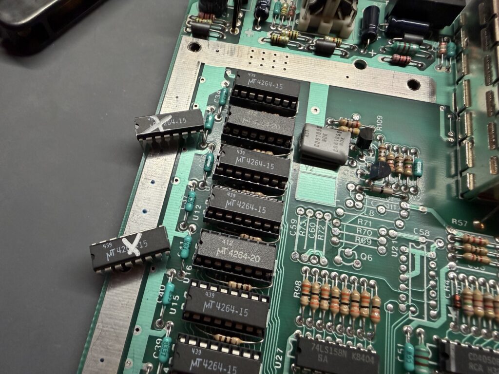 a closeup of a PCB on a workbench. two RAM chips have been removed and marked with silver Xs